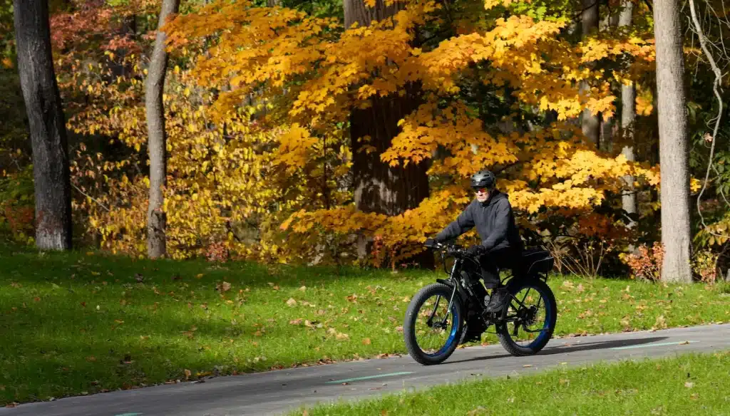 A man rides his bike against a backdrop of yellow Autumn leaves.